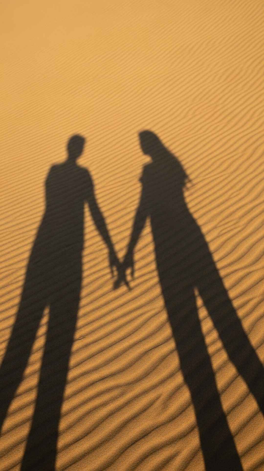 An abstract and symbolic image of a couple's shadows merging into one on a textured sand dune, representing unity and connection.