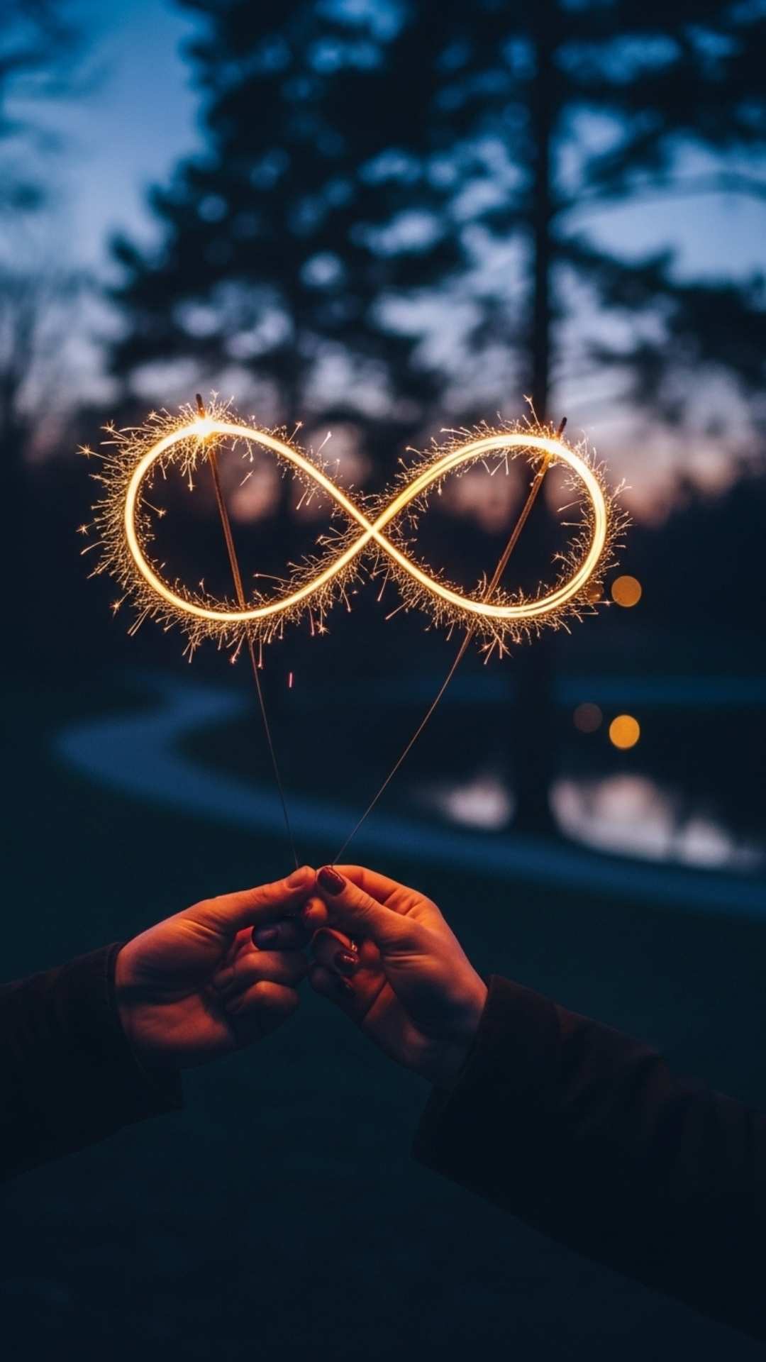 A photo of an infinity sign drawn with a sparkler at dusk, held by a couple's hands