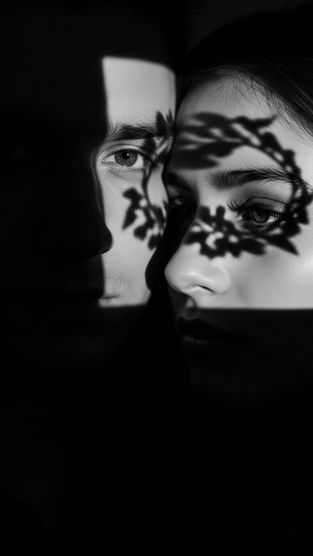 A high-contrast, black and white portrait of a couple with abstract shadows across their faces, creating an artistic and mysterious mood