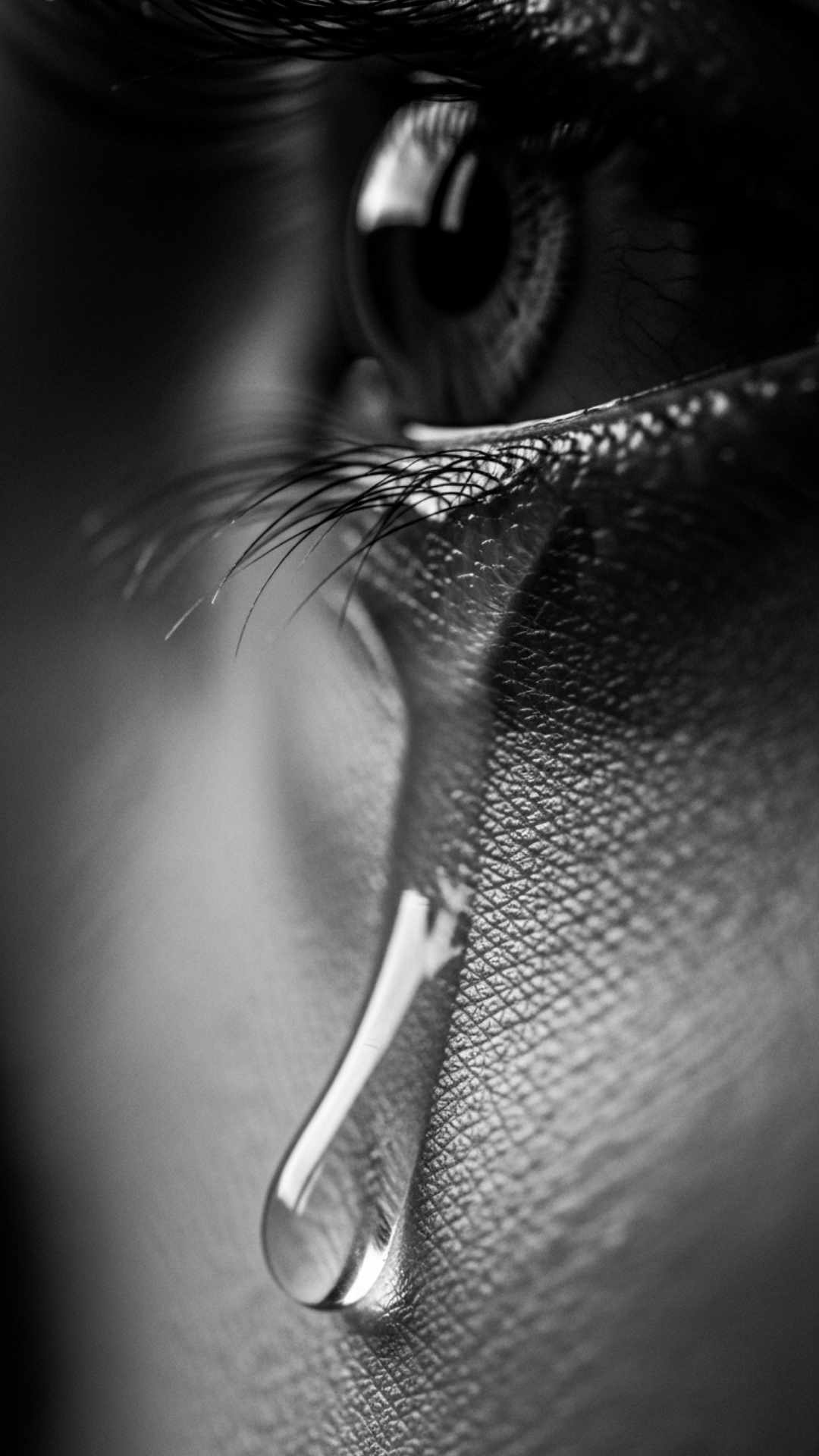 A cinematic, black-and-white close-up of a single tear rolling down a person's cheek. The tear is in sharp focus, conveying a raw and emotional sense of sorrow.