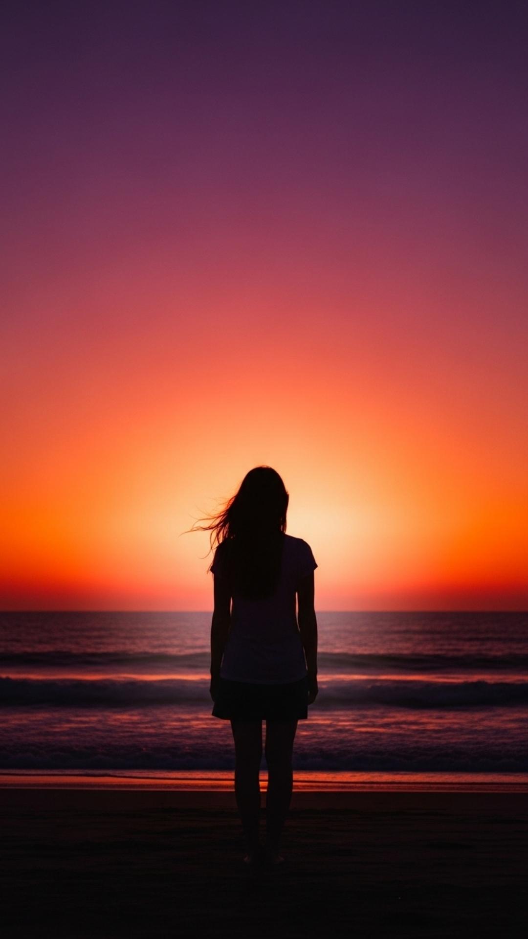 A silhouette of a young woman standing alone on a beach against a fiery sunset
