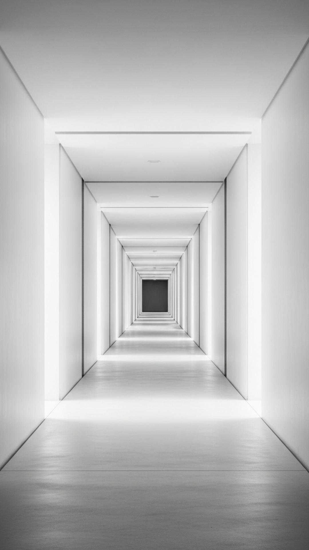 A starkly lit, empty corridor with converging lines, suggesting a feeling of emptiness and detachment. The image is minimalist and desaturated in color.
