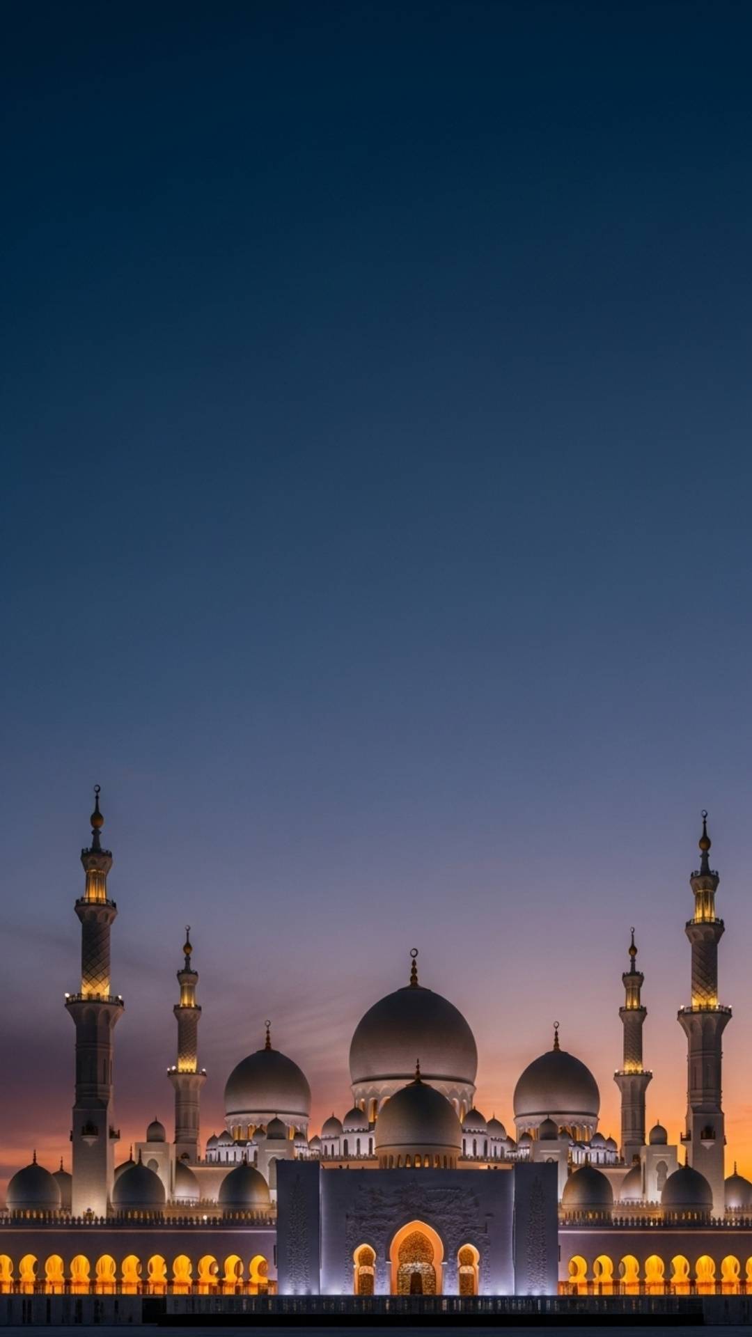 A breathtaking photograph of a grand mosque at dusk, with its minarets and domes illuminated in warm light against a twilight sky