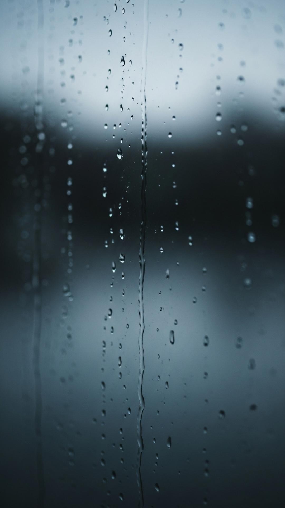 A close-up photo of raindrops on a window pane, with a blurry and muted background, creating a moody and reflective atmosphere.