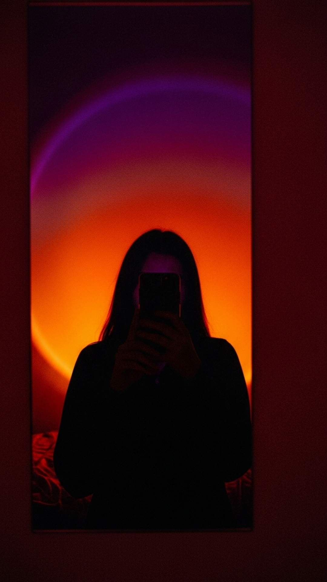 An artistic hidden face mirror selfie taken with sunset lamp lighting to create a mysterious silhouette. This grainy, lo-fi aesthetic image captures a specific mood and vibe, popular among Gen Z for emotional or abstract profile pictures on social media platforms like TikTok and Pinterest.