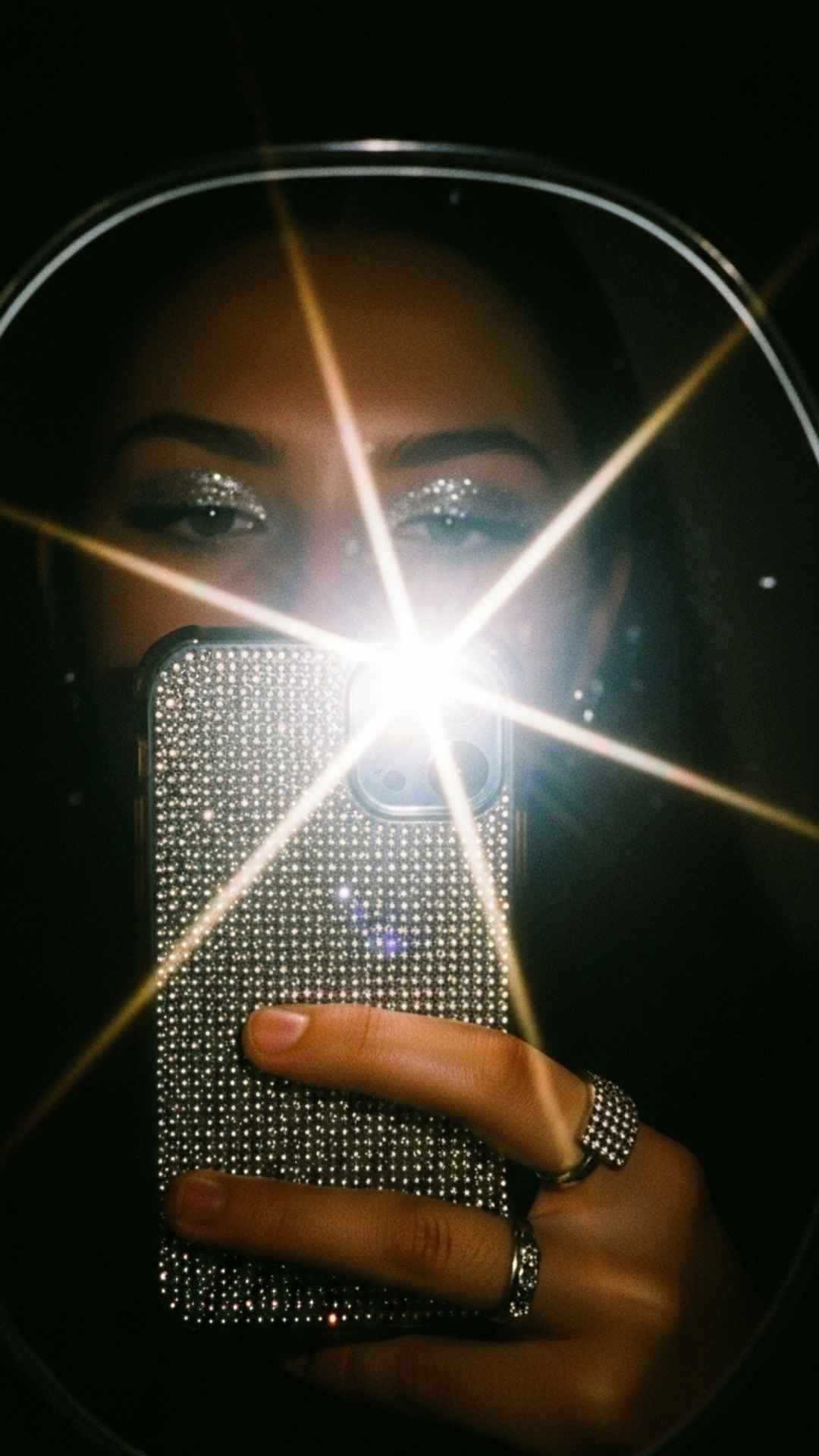 A close-up high-contrast mirror selfie using a flash to highlight sparkling accessories and Y2K details. The image features a nostalgic, grainy texture perfect for an aesthetic Instagram DP, focusing on the "flash aesthetic" trend where the bright light creates a dramatic, moody effect against a dark background.