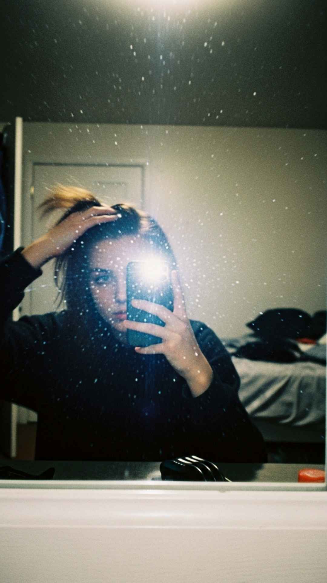 A raw and authentic lo-fi mirror selfie with motion blur and flash, capturing a candid moment. This high-contrast, grainy photo style is ideal for users seeking an edgy, "off-duty" profile picture (DP) that feels unposed and vintage, embracing the imperfection of film photography.