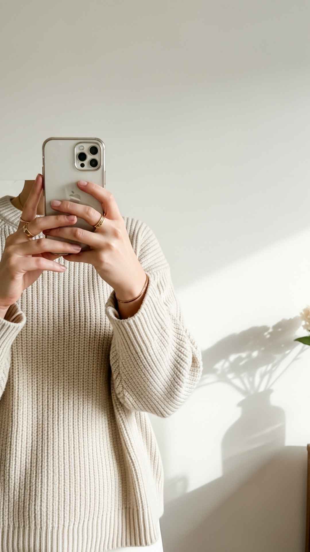 A close-up vertical aesthetic mirror selfie highlighting "quiet luxury" details like a cream sweater and minimal gold jewelry. This neutral-toned image focuses on a clutter-free composition and soft lighting, serving as perfect inspiration for an anonymous, elegant display picture (DP) on social media.
